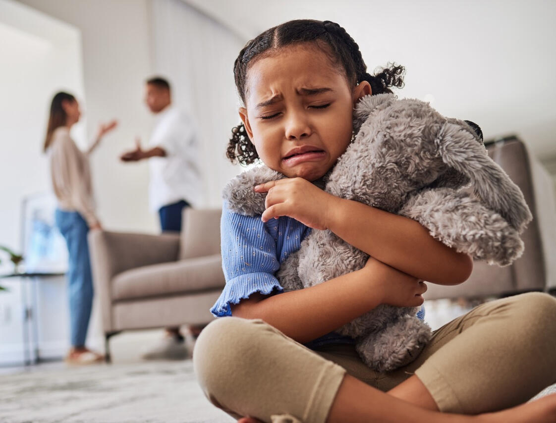 Child Caught in the Middle of a Family Law Dispute A young girl clutching a stuffed animal and crying while her parents argue in the background, representing child custody and family law investigation services by West Coast Private Investigators in Rancho Santa Margarita, CA.